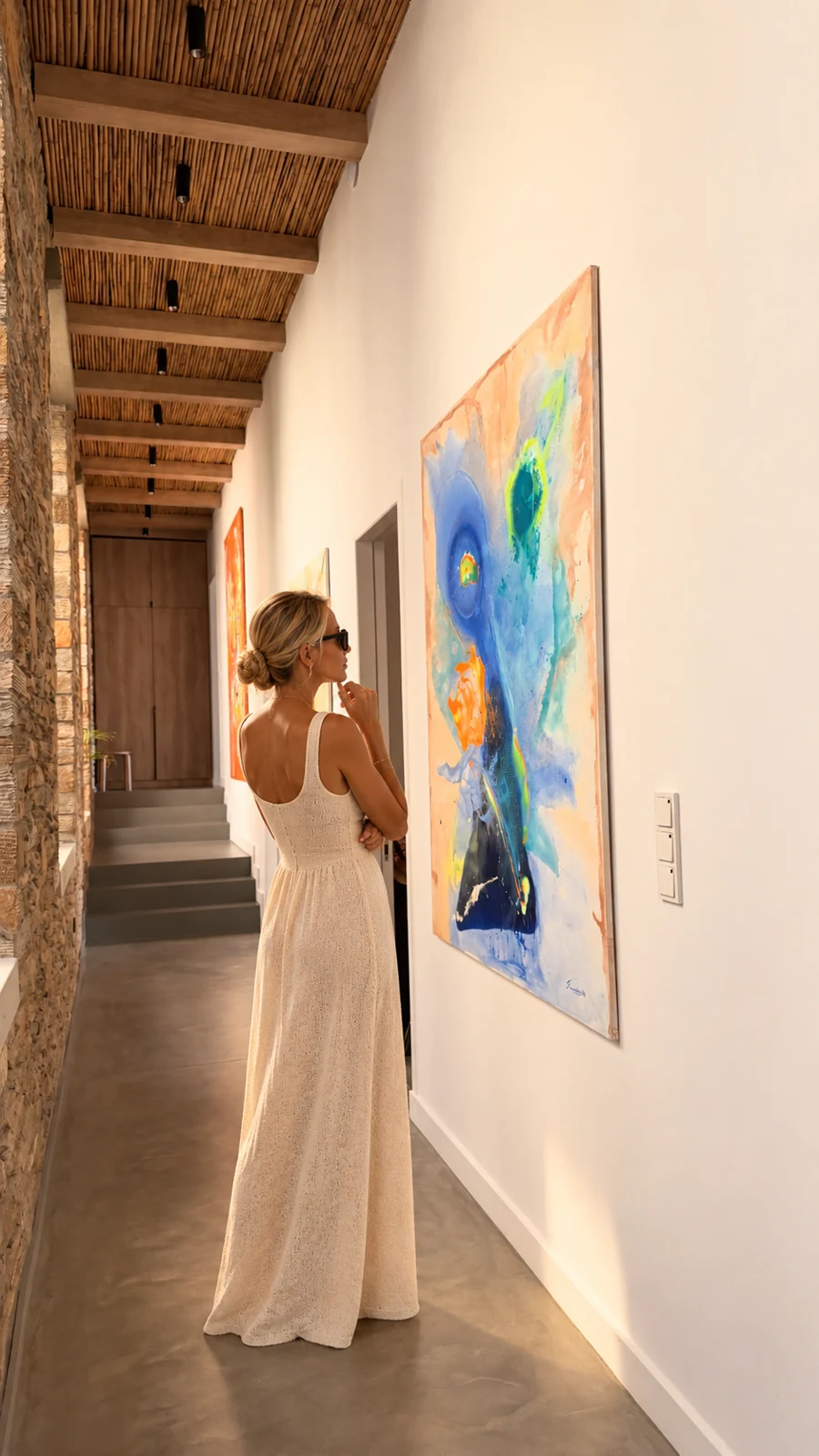 A woman looking at abstract artwork in the stone-lined villa hallway